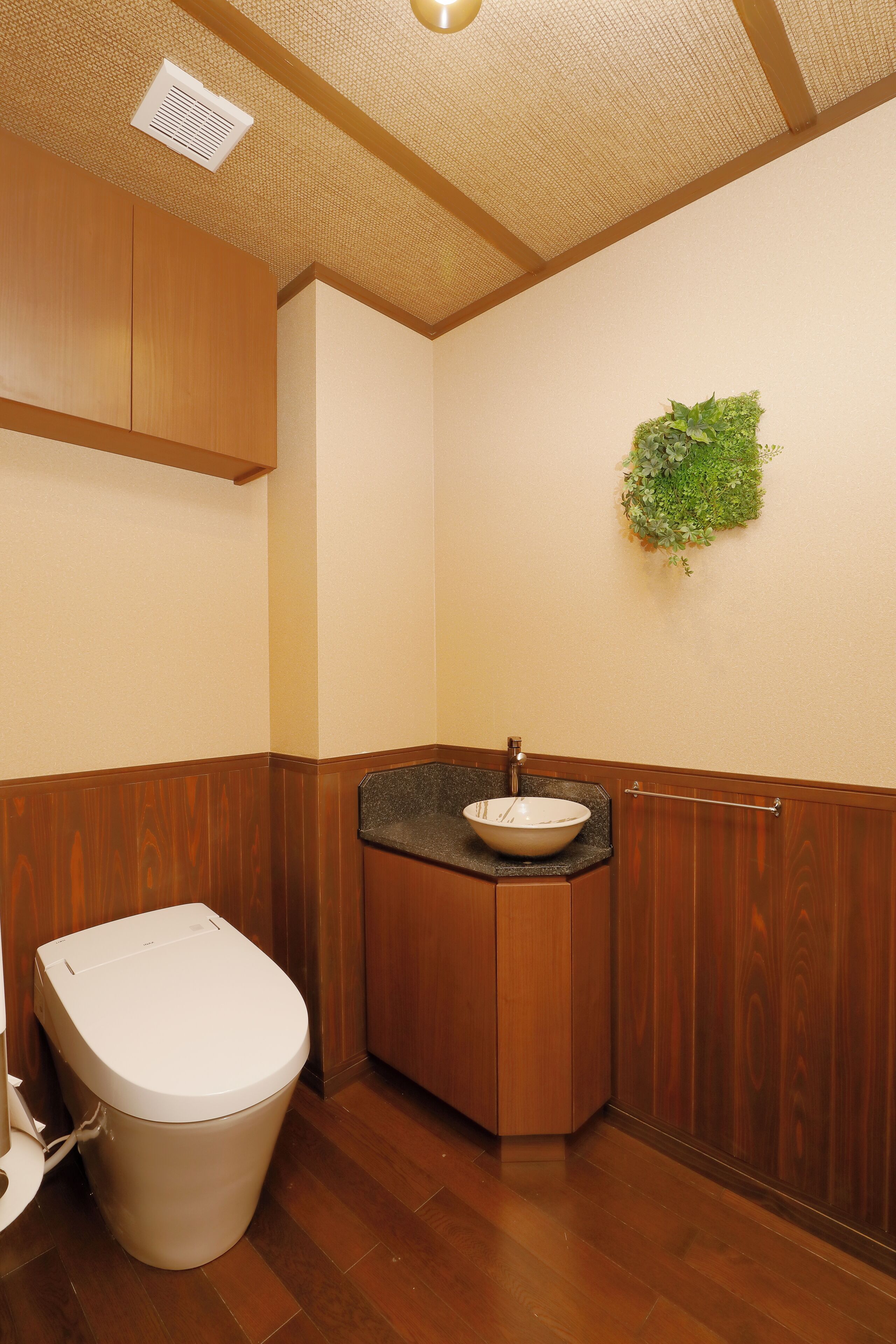 Une salle de bain avec un meuble-lavabo en bois, des toilettes blanches et un élément décoratif vert sur le mur.