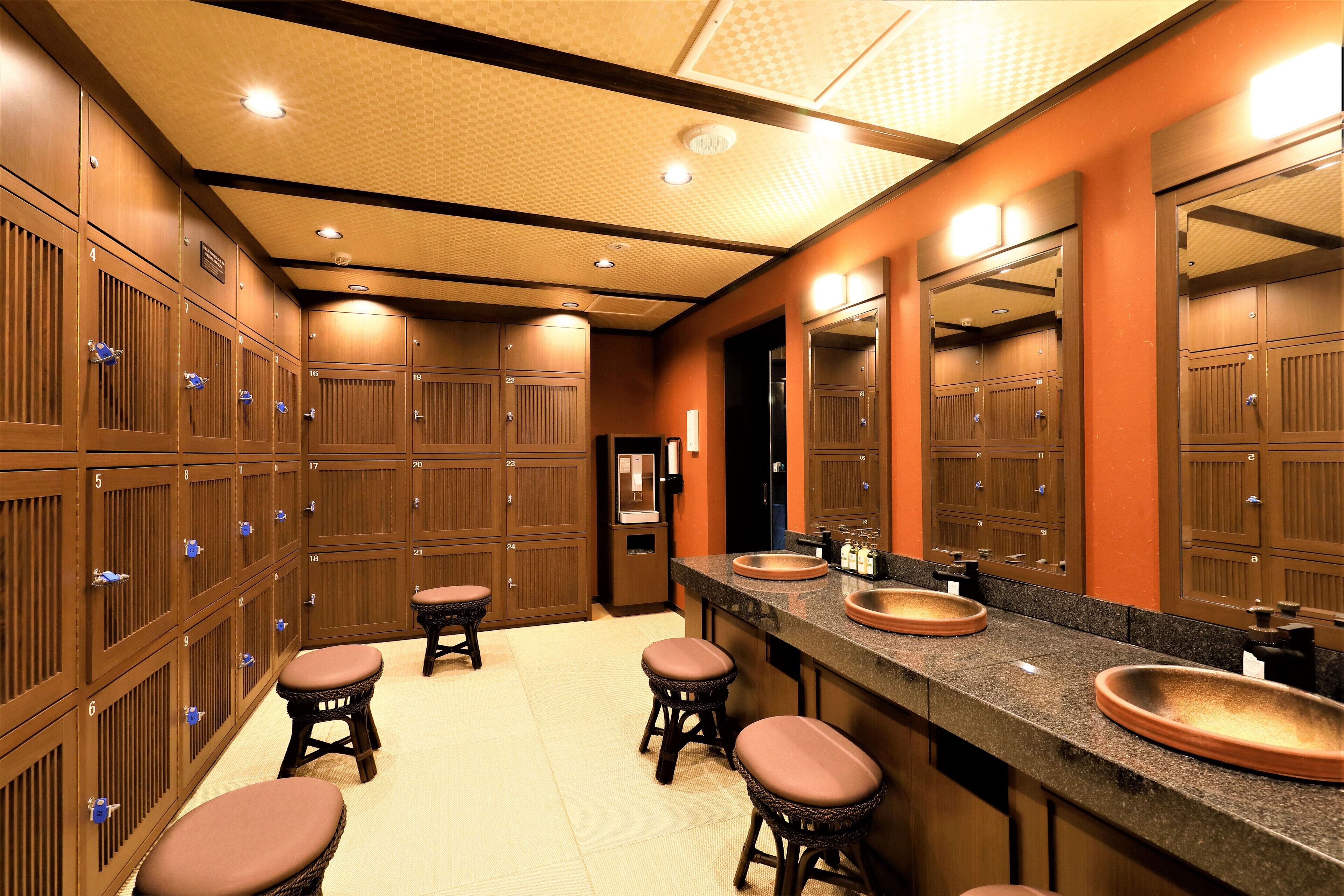 A hotel bathroom with multiple lockers, sinks, and stools.
