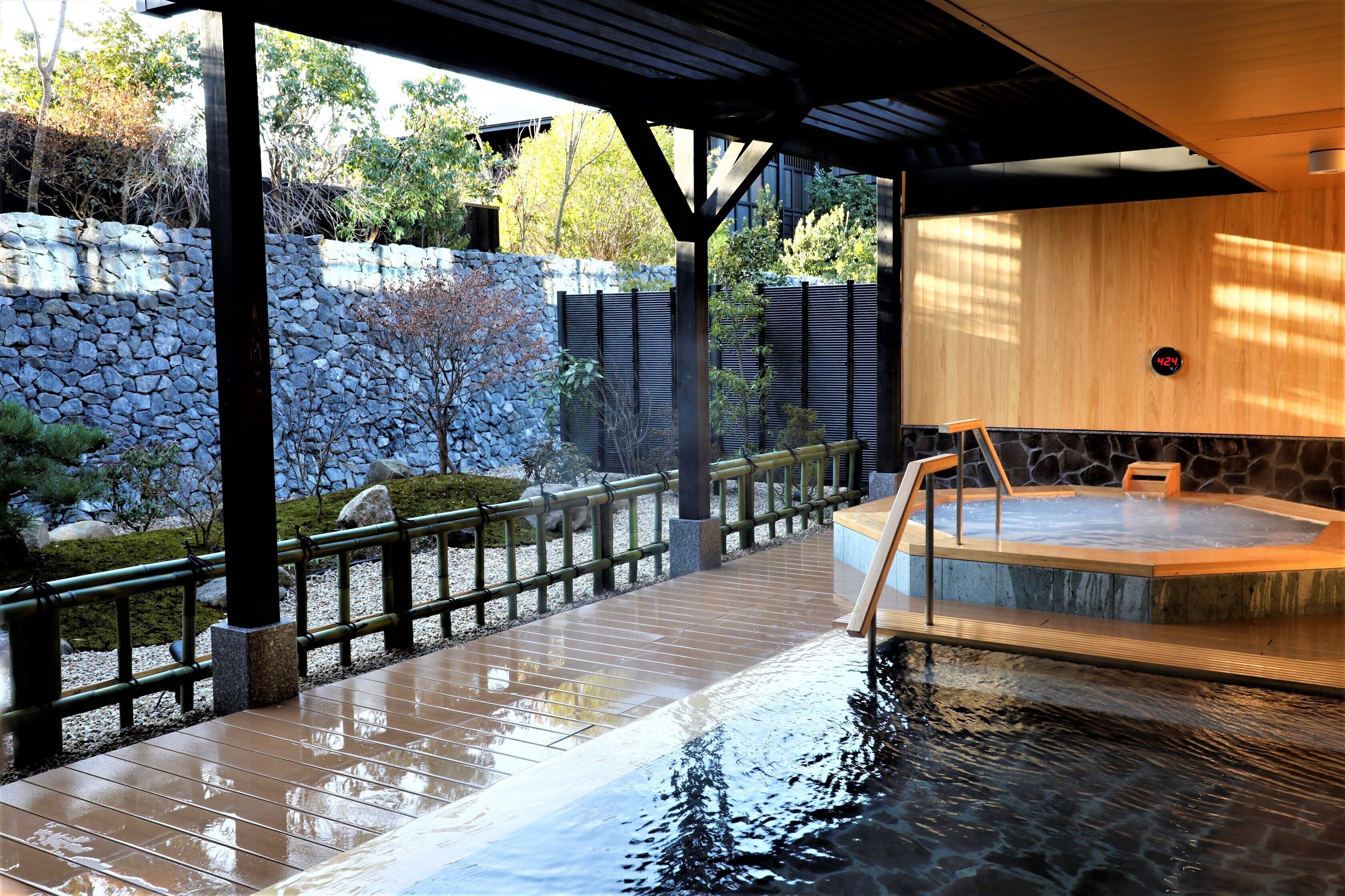 A hot spring area with a wooden deck, stone wall, and a wooden cabin.