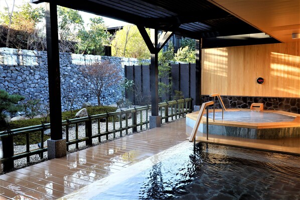 A hot spring area with a wooden deck, stone wall, and a wooden cabin.