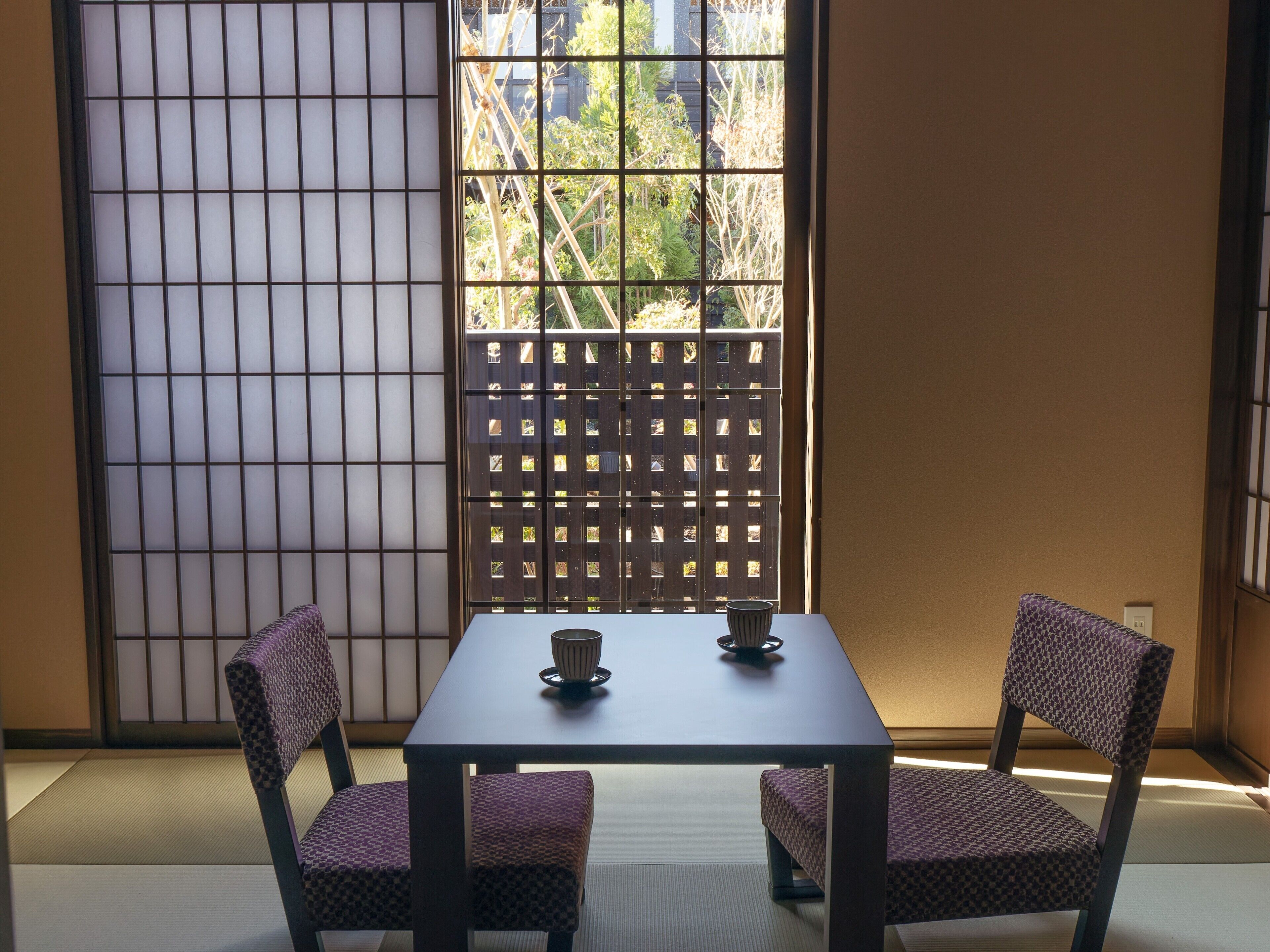 A traditional Japanese room with tatami flooring, a shoji screen, and a low table with two chairs.