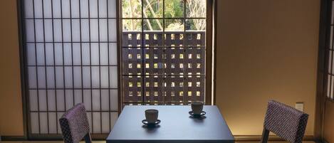 A traditional Japanese room with tatami flooring, a shoji screen, and a low table with two chairs.