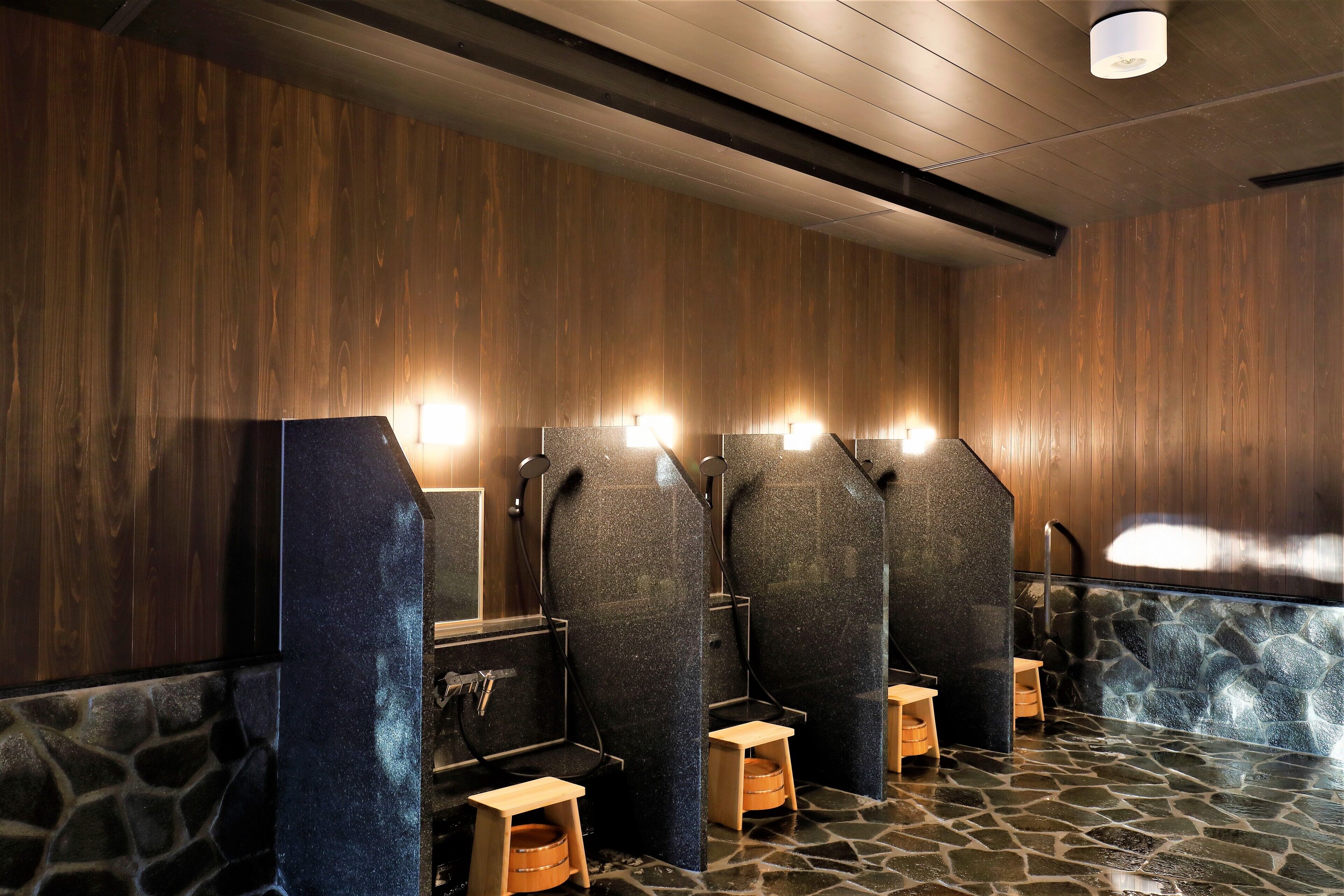 A public restroom with wooden walls, stone flooring, and multiple sinks with overhead lighting.