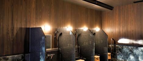 A public restroom with wooden walls, stone flooring, and multiple sinks with overhead lighting.