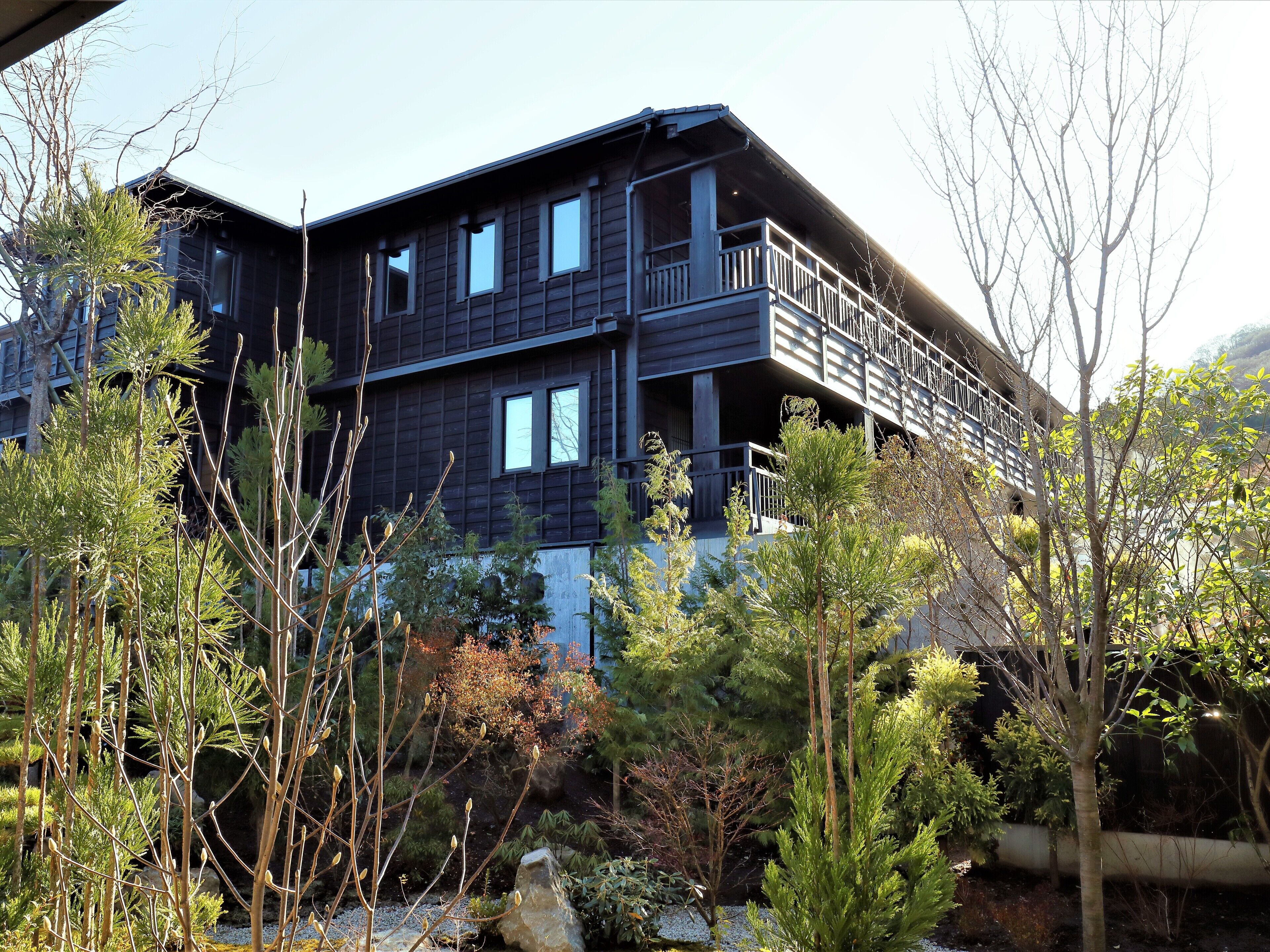 A multi-story building with balconies, surrounded by various trees and shrubs.