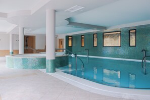 A modern indoor swimming pool with clear glass walls, tiled floors, and a central staircase leading to upper levels. - BEST OF BOTH (Divonne-les-Bains)