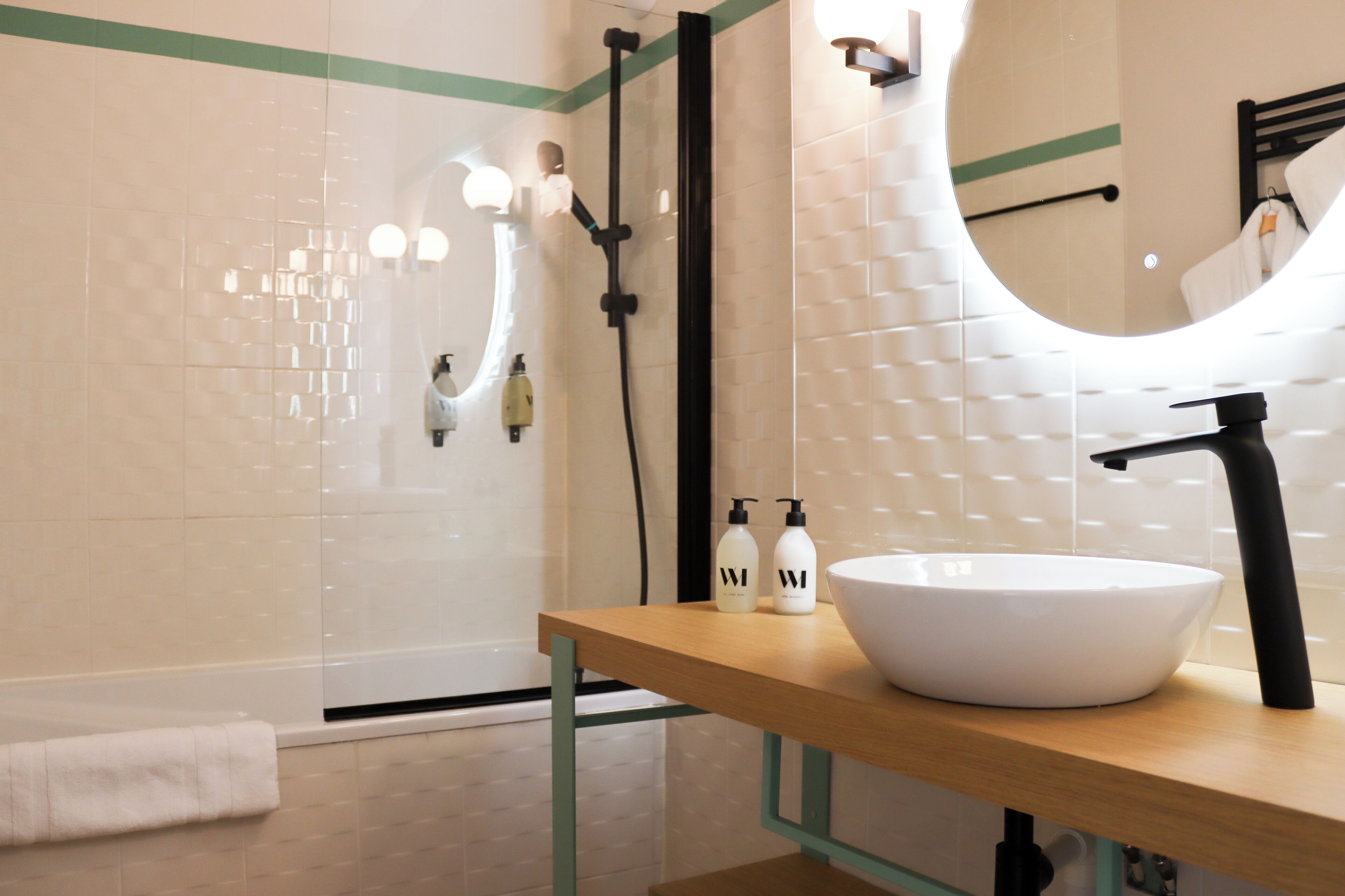 A modern bathroom with a white sink, black faucet, and a wooden vanity. There are two bottles of shampoo and conditioner on the vanity.