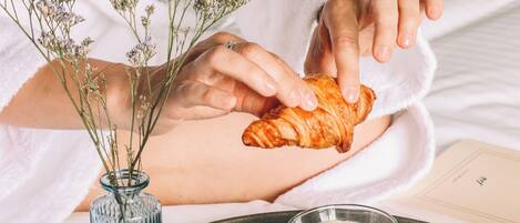 Ein Tablett mit Croissants, einer Kaffeetasse und einer Blumenvase auf einem Bett.