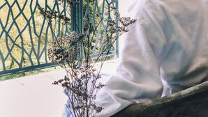 A person sitting on a chair by a window with a view of trees and a decorative vase with flowers. - BEST OF BOTH (Divonne-les-Bains)