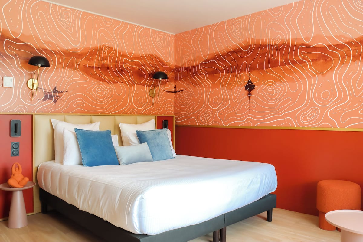 Quarto moderno com uma cama grande, duas luminárias de cabeceira e um design de parede laranja original.