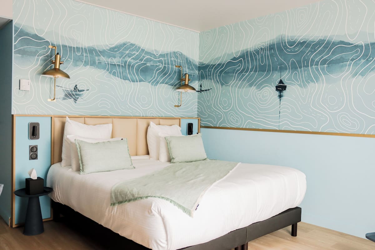 Quarto com cama, duas luminárias de cabeceira, mesa de cabeceira e parede com design topográfico.