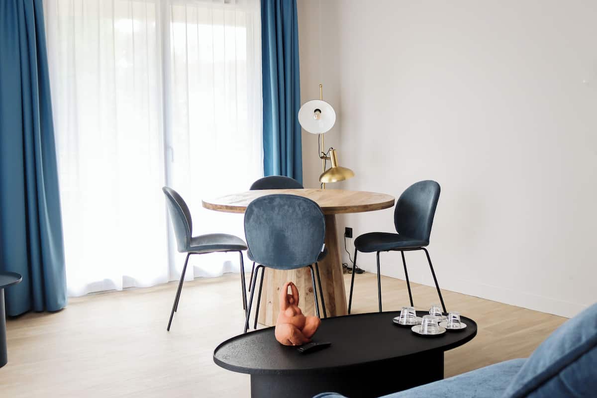 Uma área de refeições moderna com uma mesa de madeira redonda, quatro cadeiras e um abajur dourado no chão.