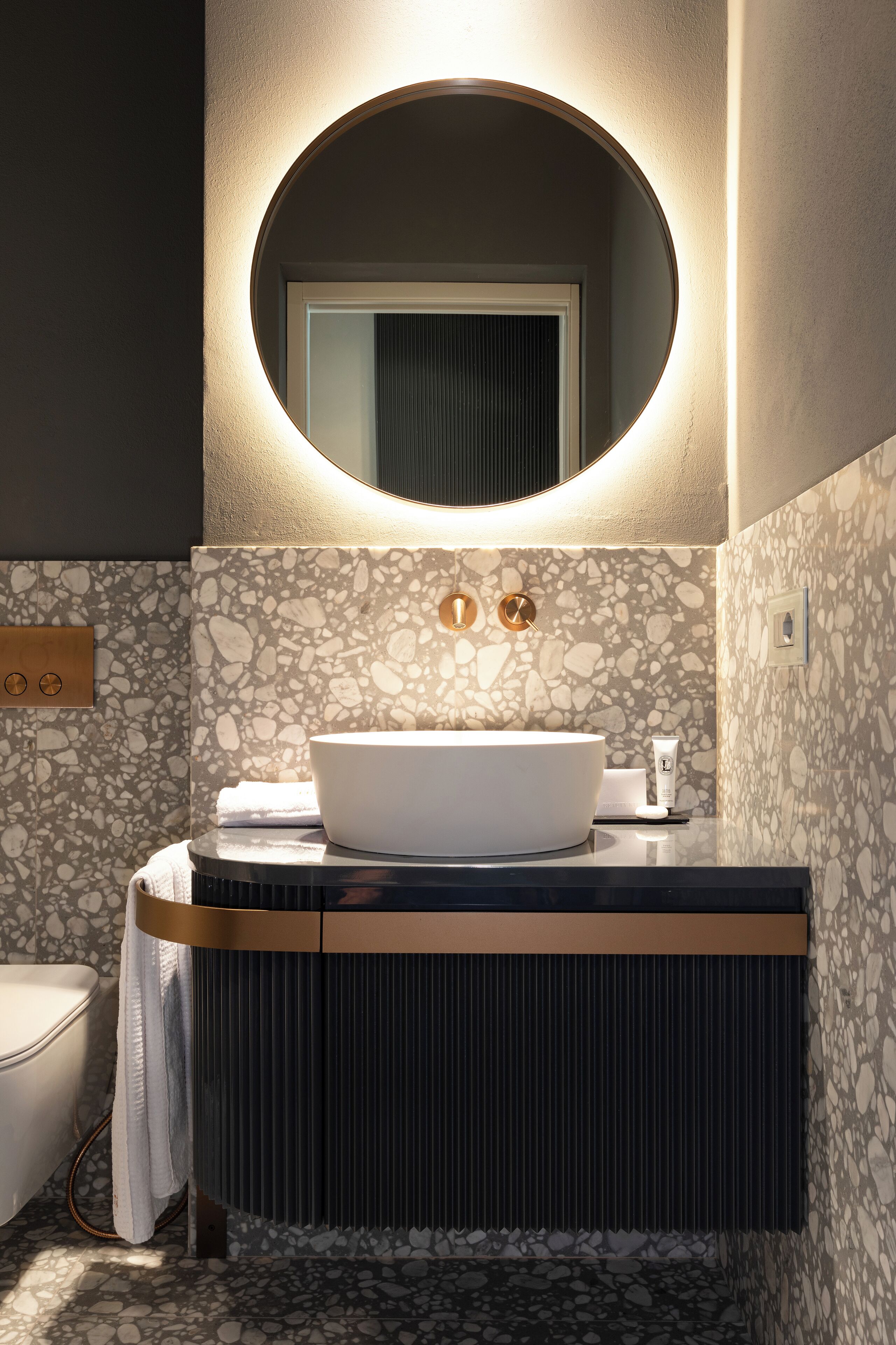 A modern bathroom with a round mirror, a white sink, and a textured wall.