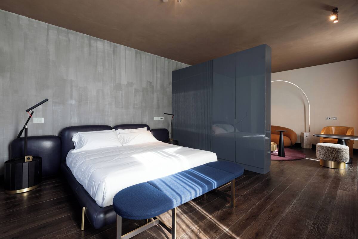 A modern bedroom with a large bed, a bench, a desk, and a chair.