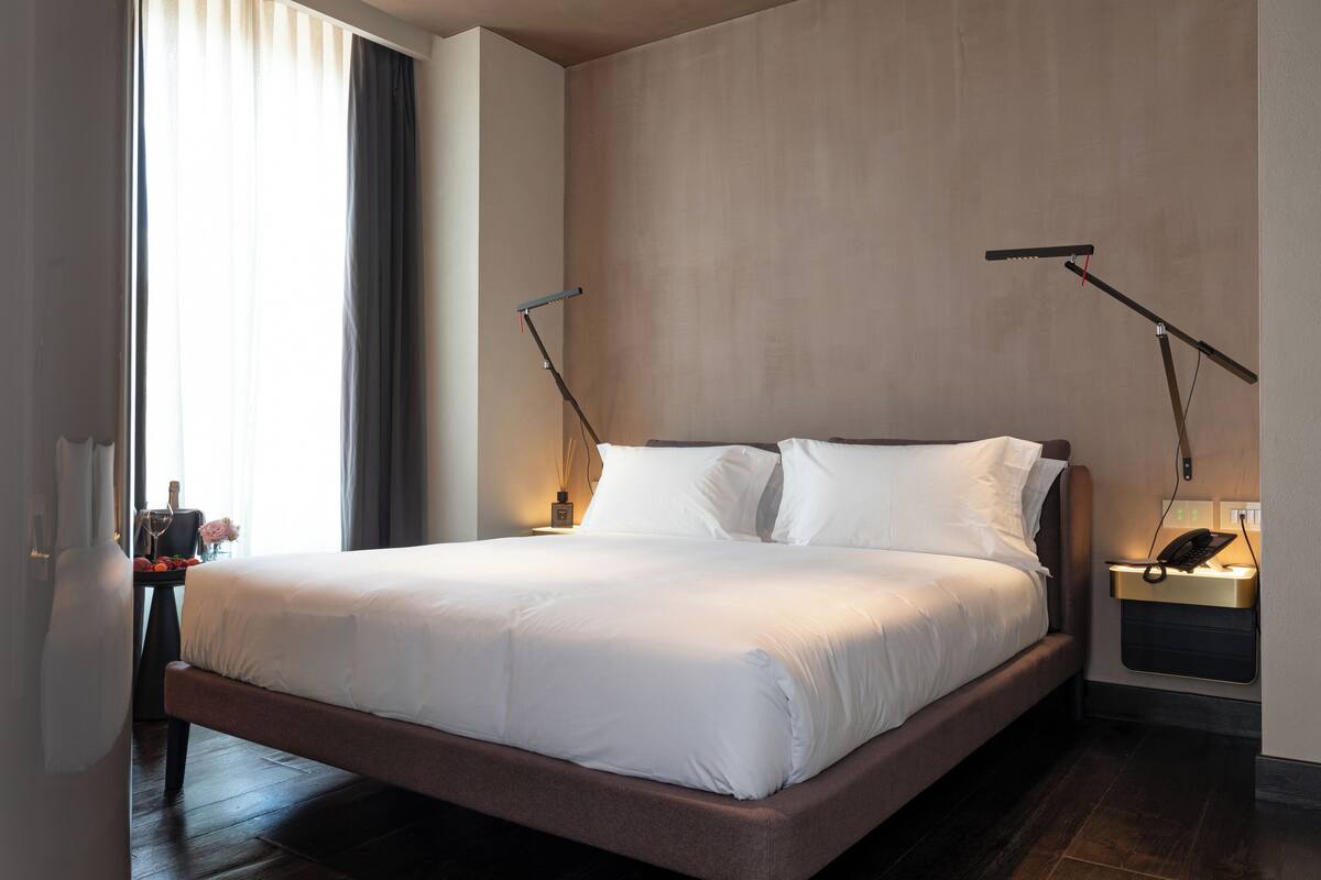 A modern hotel room with a large bed, bedside lamps, a nightstand, and a wall-mounted phone.