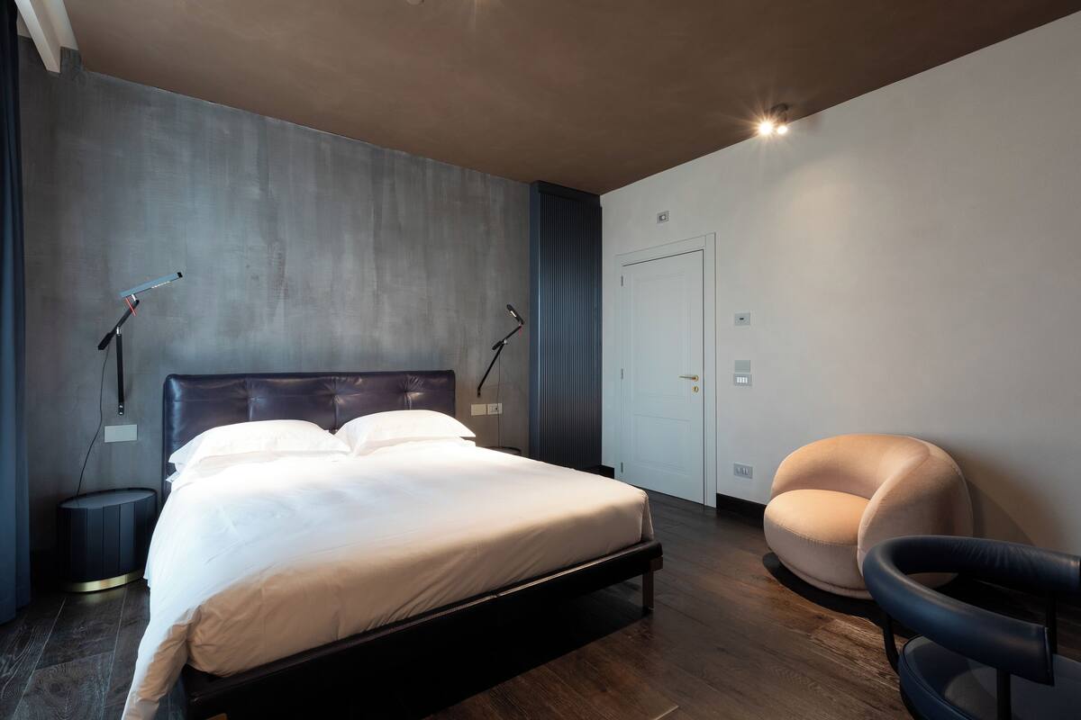 A modern bedroom with a large bed, bedside lamps, a round chair, and a wardrobe.