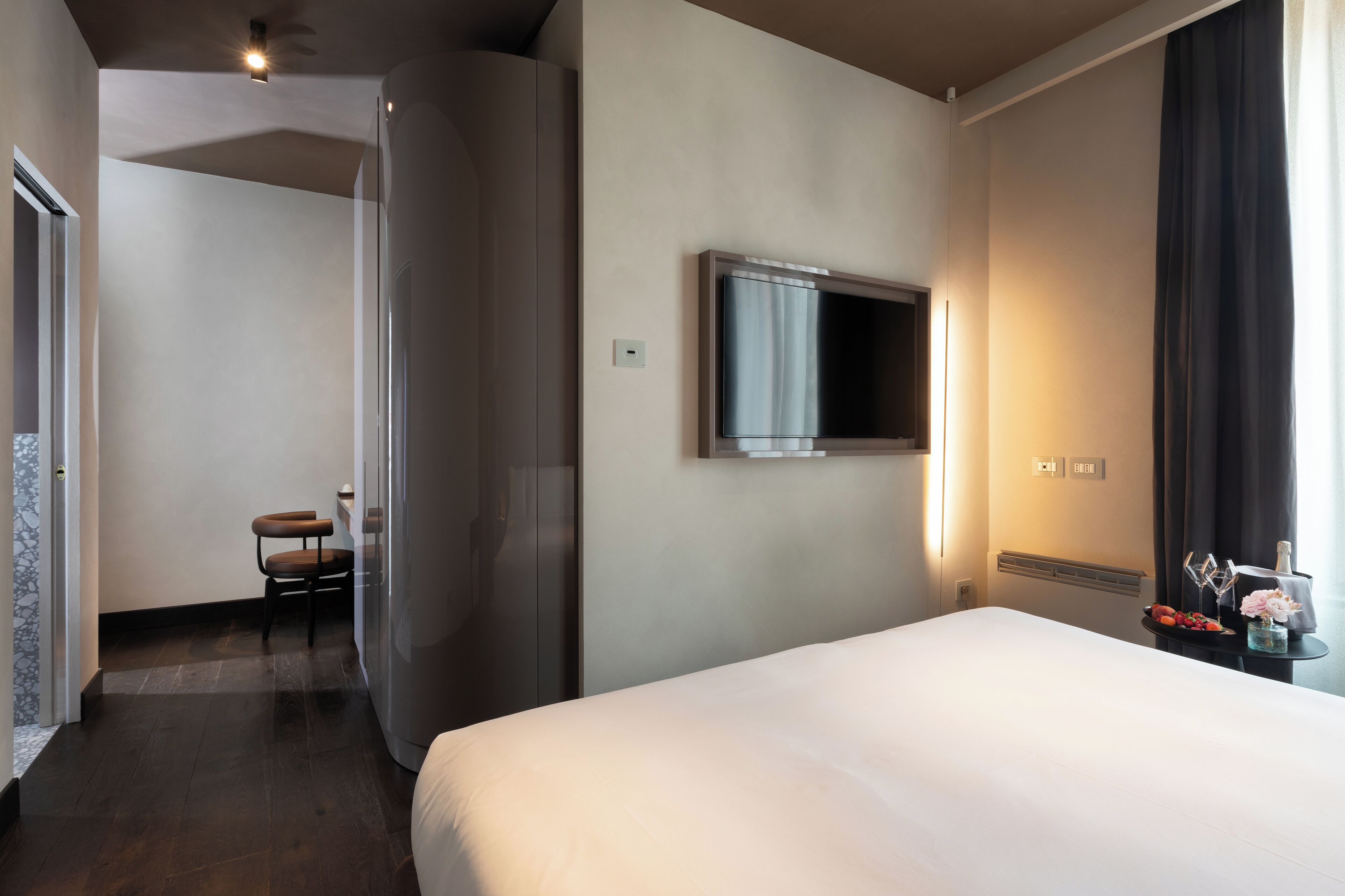 A hotel room with a large bed, a television mounted on the wall, a small table with a vase and flowers, and a chair.
