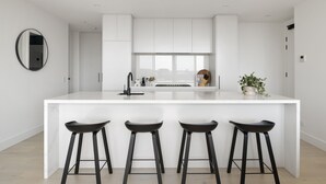 Una cocina moderna con una isla blanca, taburetes negros y un amplio ventanal.