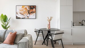 Una sala moderna con un sofá gris, una mesa de comedor redonda y una cocina con armarios blancos.