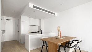 Una cocina moderna con armarios blancos, una mesa de comedor de madera y sillas negras.