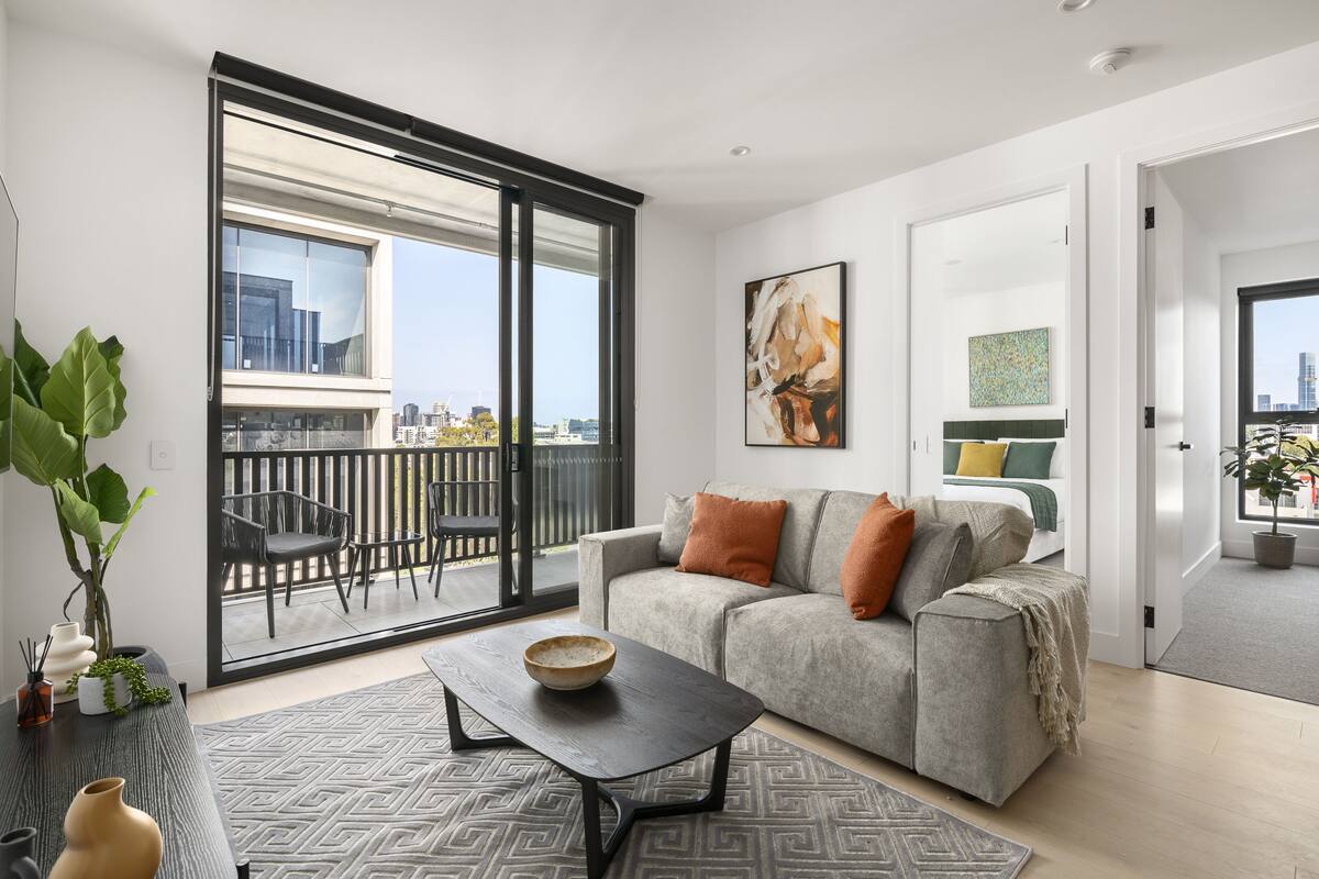 A modern living room with a grey sofa, a black coffee table, and a large window with a city view.