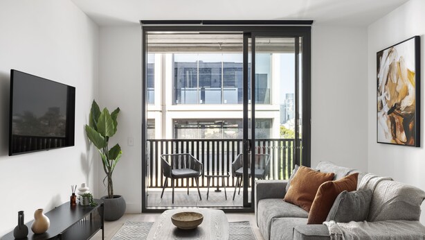 Un salón moderno con un sofá gris, una mesa de centro y un ventanal con vistas a un paisaje urbano.