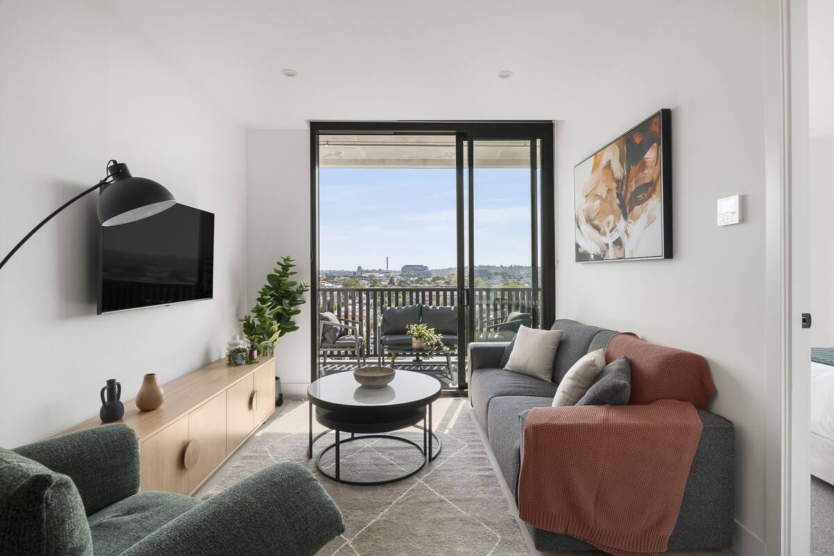 A modern living room with a sofa, a coffee table, a TV, and a balcony with a city view.