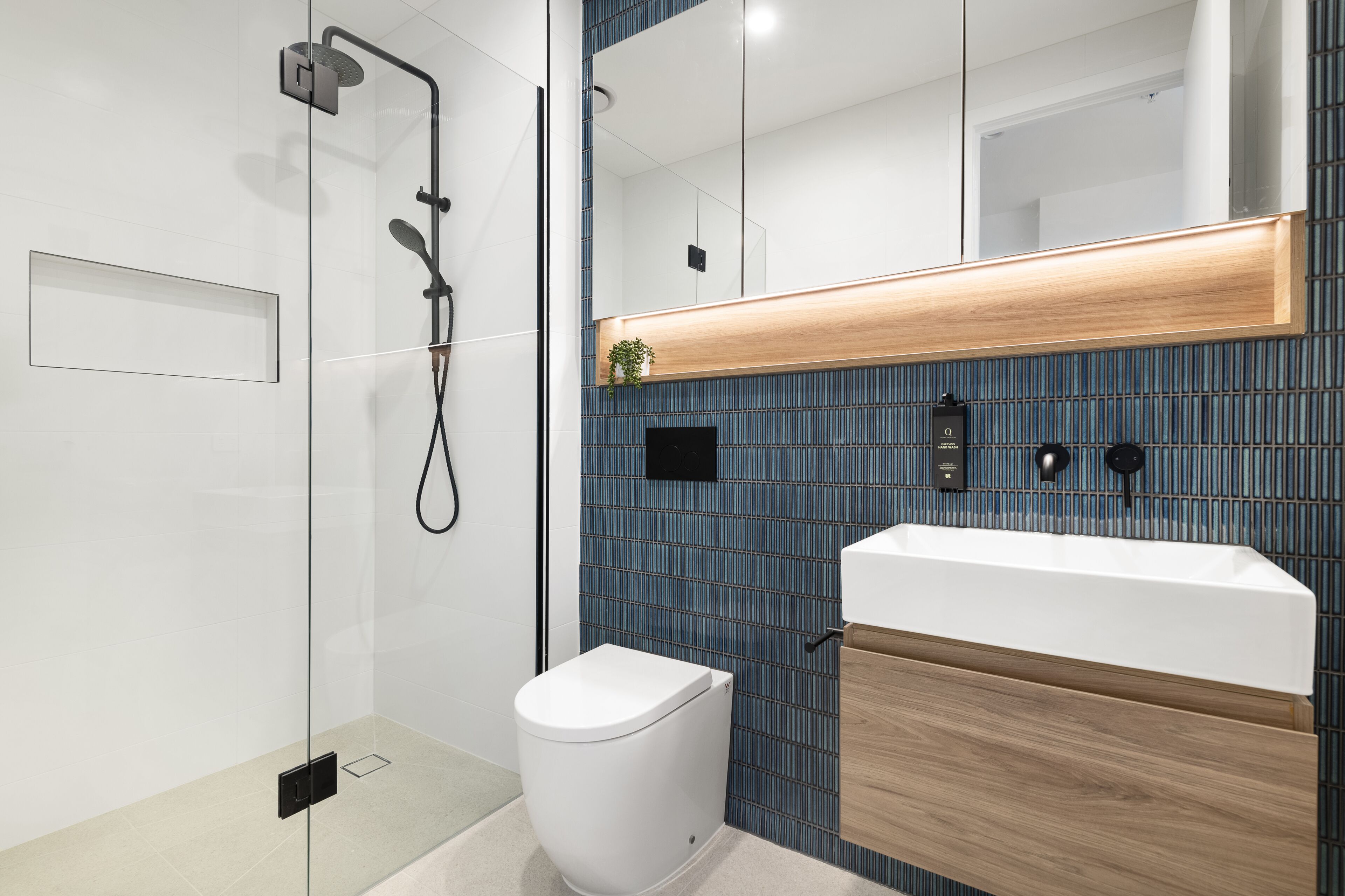 A modern bathroom with a glass-enclosed shower, a white toilet, and a wooden vanity with a sink.