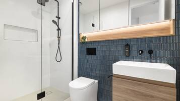 A modern bathroom with a glass-enclosed shower, a white toilet, and a wooden vanity with a sink.