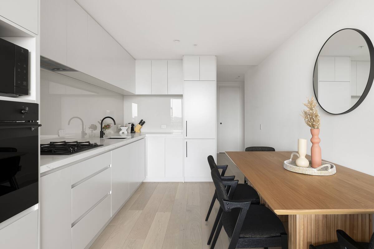 A modern kitchen with white cabinets, a wooden dining table, and a large mirror on the wall.