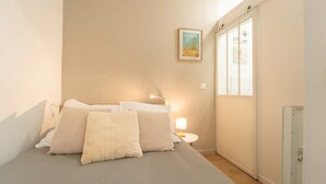 Une chambre à coucher avec un lit, des oreillers, une table de chevet avec une lampe, un tableau encadré au mur et une fenêtre avec des stores.