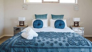 Ein Schlafzimmer mit einem Bett, zwei Nachttischen, zwei Lampen, einem Fenster und dekorativen Wandschildern.