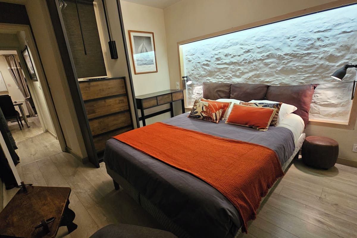 A bedroom with a bed, a window with a view of the sea, a desk, and a chair.