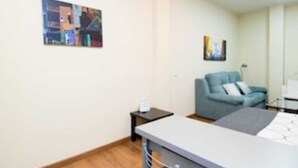 A hotel room with a bed, a small table, a chair, a sofa, and two paintings on the wall. - Madrid - Studio Gran via 1C (Madrid)