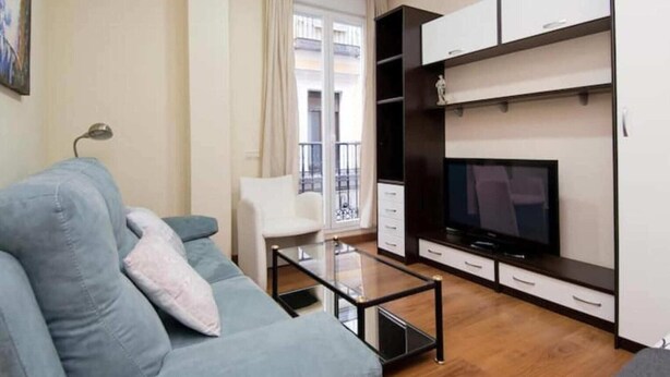 A modern living room with a grey sofa, a glass coffee table, a TV on a wooden stand, and a white chair. - Madrid - Studio Gran via 1C (Madrid)