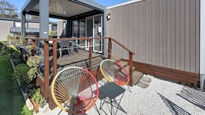 A modern outdoor patio with a wooden deck, two colorful chairs, and a covered seating area. - Luxury Mobile Home for 6, Heated Pool, 200m from Beach (Jullouville)