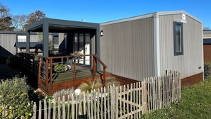 A modern, compact mobile home with a covered porch, a small deck, and a fenced garden area. - Luxury Mobile Home for 6, Heated Pool, 200m from Beach (Jullouville)