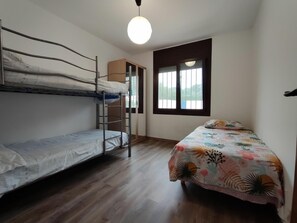 Een kamer met twee stapelbedden, een houten garderobe, een raam met zonwering en een hanglamp.