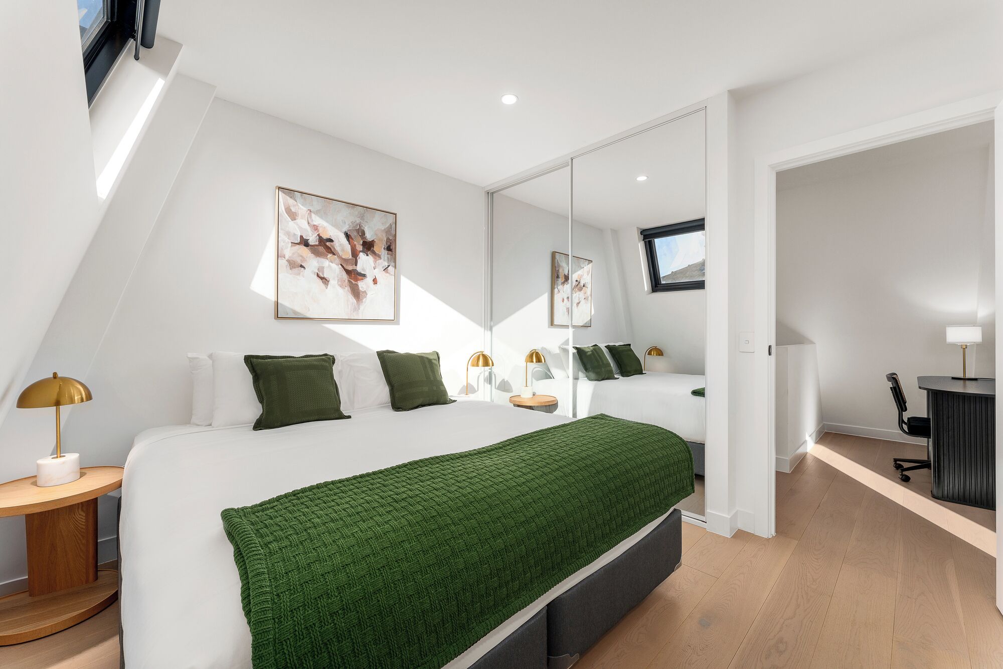 A modern bedroom with a large bed, a side table, a mirror, and artwork on the wall.