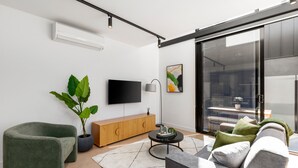 A modern living room with a flat-screen TV, a potted plant, a wooden cabinet, and a sofa. - Fitzroy North Apartments by Urban Rest (Clifton Hill)