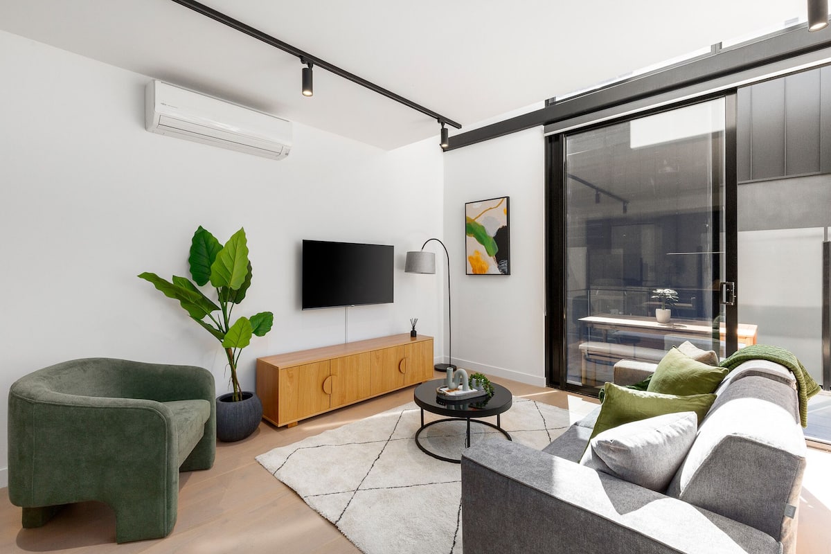 A modern living room with a flat-screen TV, a potted plant, a wooden cabinet, and a sofa.