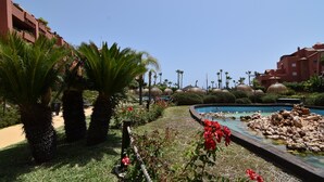 A resort pool area with palm trees, a small pond, and red flowers. - Quiet and Luxurious Apartment on the Beach (Torrox)