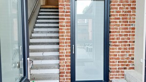 A staircase leading to a door with a metal handle, a glass door, and a brick wall. - "Lindenblatt" 3-room apartment, 2 bathrooms, Büsum (4km), parking lot, North Sea (Oesterdeichstrich)