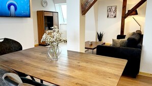 A modern living room with a wooden dining table, a sofa, a TV mounted on the wall, and a staircase. - "Lindenblatt" 3-room apartment, 2 bathrooms, Büsum (4km), parking lot, North Sea (Oesterdeichstrich)