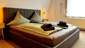 A neatly made bed with pillows, a bedside lamp, and a window with curtains. - "Lindenblatt" 3-room apartment, 2 bathrooms, Büsum (4km), parking lot, North Sea (Oesterdeichstrich)