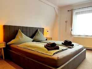 A neatly made bed with pillows, a bedside lamp, and a window with curtains.