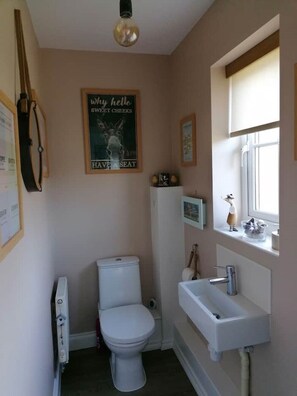 Un baño pequeño y bien iluminado, con inodoro, lavamanos y un cartel en la pared.