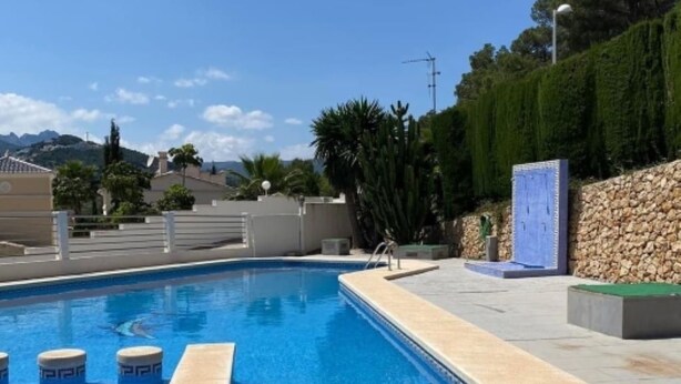 A swimming pool with clear blue water, surrounded by a stone wall and greenery.