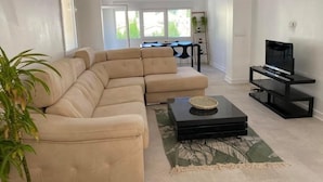 A living room with a beige sectional sofa, a black coffee table, and a TV on a black stand.