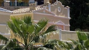 A building with a tiled roof and a white facade, surrounded by palm trees.